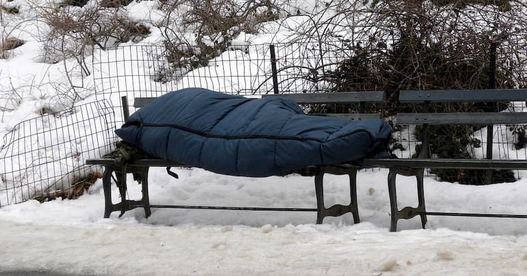 Homeless person sleeping on a bench in the snow