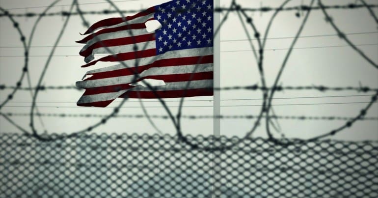 A tattered American flag behind razor wire