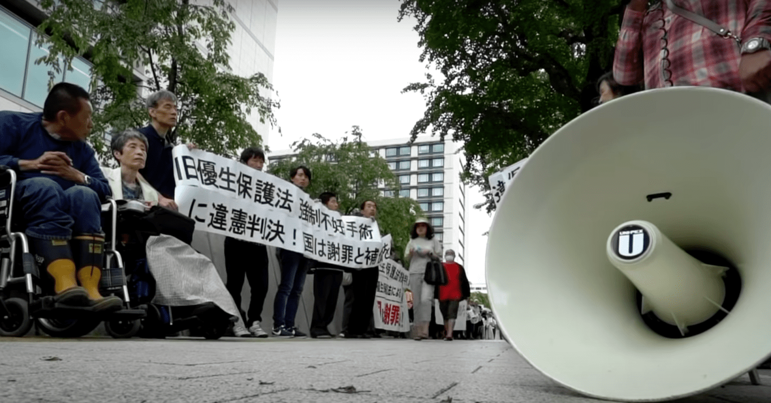 A protest with people standing in a line - the protest is against Japan's forced sterilisation laws and aftermath