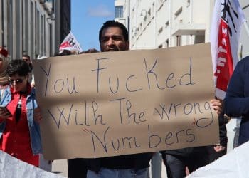 A greek call centre worker holding a placard that says you fucked with the wrong numbers