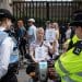 Disabled man Neil Goodwin protesting in his mobility scooter at the entrance to parliament. He is surrounded by police officers and holding signs that read "disabled people against climate change" and ""I cannot run from a climate emergency"