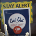 Eat out to help out poster, with a sign behind saying "stay alert".