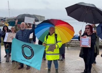 Protesters stand in the rain at Portland port with placards that read: "no floating prison" and "asylum process - EU: 6-9 months - UK: 1-3 years - stuck in limbo". bibby Stockholm Labour