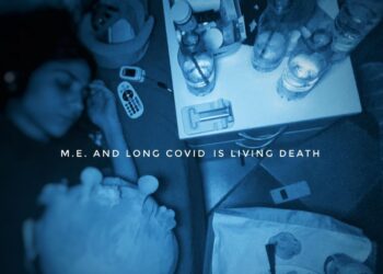 Blue-tinted image of Katiana lying in bed, her bedside table and adjacent mattress stacked out with water bottles, medication, a pulsometer, and a remote control. A plush toy is beside her, and an empty plate with a fork is next to her bed on another small table. Text overlaying it says "M.E. and Long Covid is Living Death" ME/CFS severe ME
