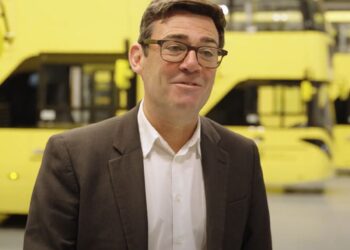 Greater Manchester mayor Andy Burnham standing in front of a fleet of yellow Bee Network buses bus fare cap