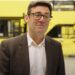 Greater Manchester mayor Andy Burnham standing in front of a fleet of yellow Bee Network buses bus fare cap