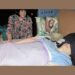 Karen Gordon, a severe ME patient, laying in bed with her eyes and ears covered as her mother looks on