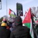 Procession of protesters in Wimborne holding placards reading "From the river to the sea, Palestine will be free" and flags. An olive branch from a local pub sign hangs out from the left of the frame, over the heads of the protesters RCV Engines Dorset