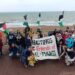 Group of people at the beach holding Palestine flags and a banner reading: "Hastings Friends of Al-Mawasi". Hastings