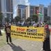 Two protesters hold a yellow banner outside DSEI reading: "Stop JCB bulldozer genocide in Palestine, India & Kashmir".