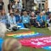 A group of Quakers sit together in pale blue t-shirts on the grass outside DSEI in silent protest.