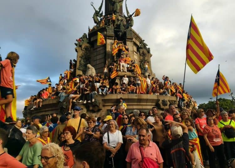 A huge crowd of people waving Catalonia's flag and climbing on a monument on La Diada.
