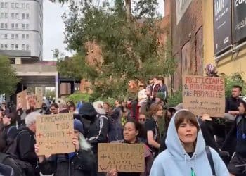 Anti-fascist counter-protesters hold placards up in a crowd reading: "Immigrants and refugees always welcome" and "Politicians and billionaires are pedophiles - and you're worried about immigrants?" Far right Newcastle