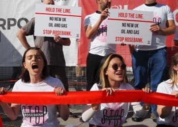 Climate protesters hold a red line in front of them, while others stand behind with placards that read "Hold the line on Rosebank. No new oil and gas".