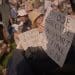 Protesters sit together holding "I oppose genocide. I support Palestine Action" placards, including an elderly woman with Palestine flag earrings Defend Our Juries