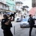 Three armed Rio de Janeiro police. Two point their guns up at a residence in the city's favelas, while one attempts to break down the door.
